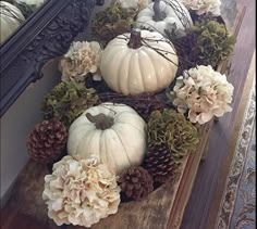 some white pumpkins and pine cones are arranged in a wreath on a mirror ledge