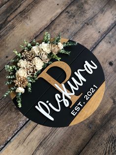 a wooden sign with flowers and greenery on it