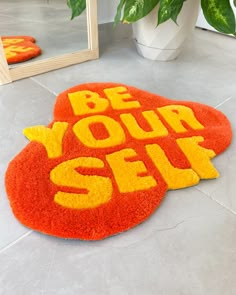 an orange and yellow rug with the words be your self on it in front of a mirror