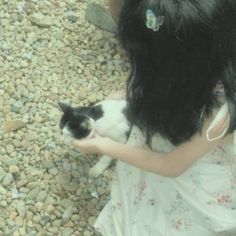 a girl holding a black and white cat in her arms while standing on some rocks