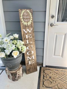 a wooden welcome sign sitting next to a potted plant on the front door steps