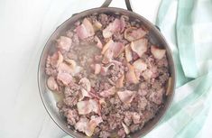 a pan filled with meat and vegetables on top of a white table next to a green towel