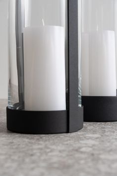 two white candles sitting inside of glass containers on a counter top next to each other