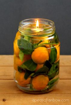 a jar filled with oranges sitting on top of a wooden table next to a lit candle