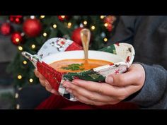 a person holding a bowl of soup in front of a christmas tree