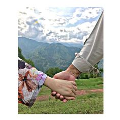 two people holding hands in the grass with mountains in the backgrouds behind them