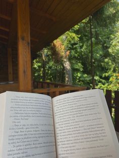 an open book sitting on top of a wooden table next to a forest filled with trees