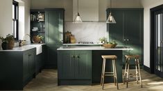 a kitchen with green cabinets and stools next to an island in the middle of the room