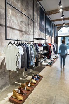 there are many shoes and shirts on display in the store with people walking by them