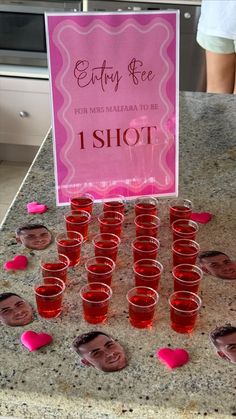 a table topped with lots of shot glasses filled with pink liquid next to a sign