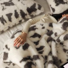 a woman laying on top of a white bed covered in black and white animal print blankets