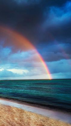 a rainbow shines in the sky over an ocean