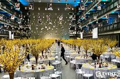 a large room filled with tables covered in white tablecloths and yellow tree decorations