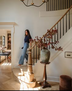 a woman is walking up the stairs in her home with an elegant vase and plant