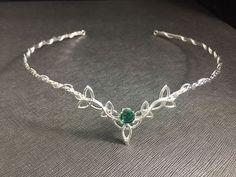 a silver bracelet with a green stone in the center on a gray surface, close up