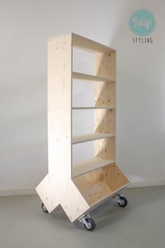 a wooden shelf sitting on top of a metal dolly in a white room with no one around it