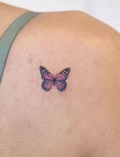 a small butterfly tattoo on the back of a woman's shoulder