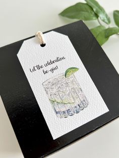 a card with a watercolor drawing of a drink and the words let the celebration be gin on it