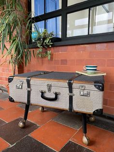 two suitcases sitting on top of each other in front of a brick building with a potted plant