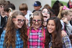 three girls are posing for the camera in front of a group of other young people