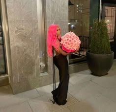 a woman with pink hair is holding a large round object in front of a building