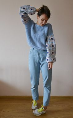 a woman standing on top of a wooden floor wearing blue jeans and a knitted sweater