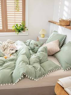 an unmade bed with green comforter and pillows on it in front of a window