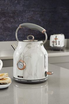 a white tea kettle sitting on top of a counter next to a plate of food