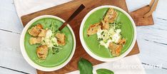 two bowls filled with green soup on top of a wooden cutting board