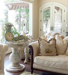 a living room filled with furniture and a clock on top of a table in front of a window