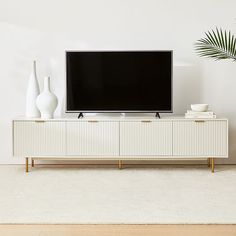 a flat screen tv sitting on top of a white cabinet next to vases and a potted plant