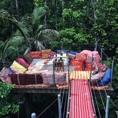 an outdoor area with lots of pillows and blankets on the ground, in front of trees