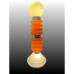 an orange and yellow light bulb sitting on top of a white lamp shade with a black background