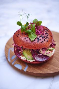 a sandwich with lettuce, tomato and sprouts on a wooden plate