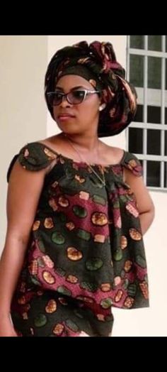 a woman wearing sunglasses and a top with an african print design on the shoulders, standing in front of a white wall