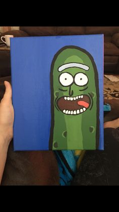 a person holding up a painting of a green cartoon character with eyes and mouth wide open