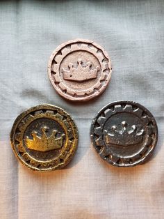 three metal buttons with crowns on them sitting on a cloth covered tablecloth in front of a window