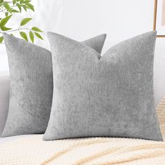 two gray pillows sitting on top of a white couch next to a potted plant