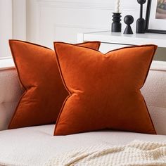 two orange pillows sitting on top of a white couch