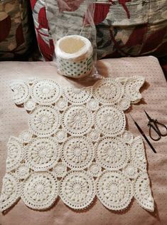 a crochet doily and some scissors on a table next to a pillow