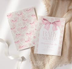 two baby shower cards with pink bows on them next to a white cloth and ribbon