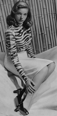 a black and white photo of a woman sitting on top of a bed with her legs crossed