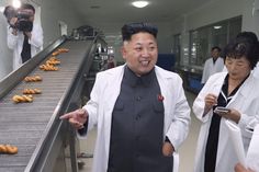 two men standing next to each other near donuts on a conveyor belt in a factory