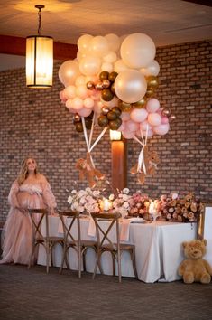 a woman sitting at a table surrounded by balloons and other decorations in front of a brick wall