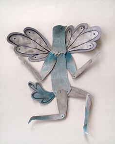 a metal sculpture of a frog with wings and legs, sitting on its back in front of a white background