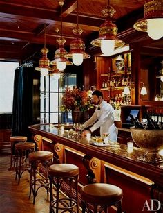 a man standing behind a bar with lots of stools and lights hanging from the ceiling