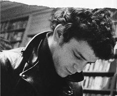 black and white photograph of a young man looking down at his cell phone in front of a bookshelf