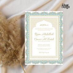 the wedding card is next to a dried plant on a white sheet with blue trim