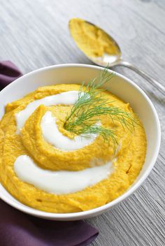 a white bowl filled with hummus next to two spoons on top of a purple napkin