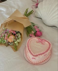 a heart shaped cake next to a bouquet of flowers on a white tablecloth covered bed